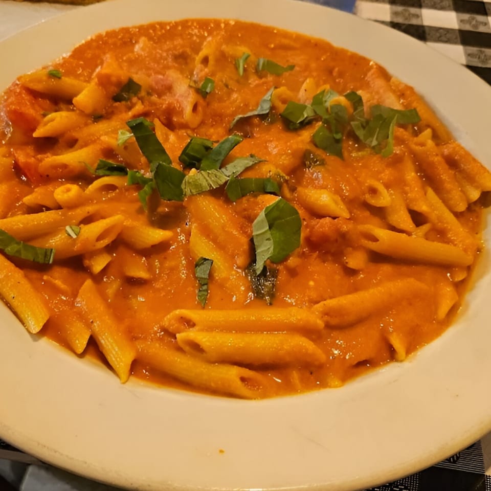 Penne pasta in a creamy tomato sauce, garnished with fresh basil, served on a white plate.