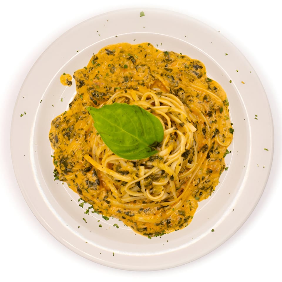 Overhead view of linguine pasta with creamy orange sauce, green herbs, and a basil leaf on a white plate.