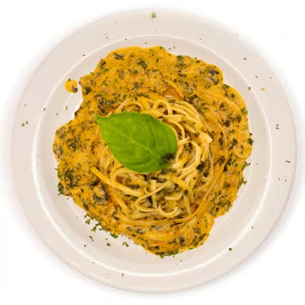 Linguine pasta with a creamy orange sauce and green herbs, garnished with a fresh basil leaf.
