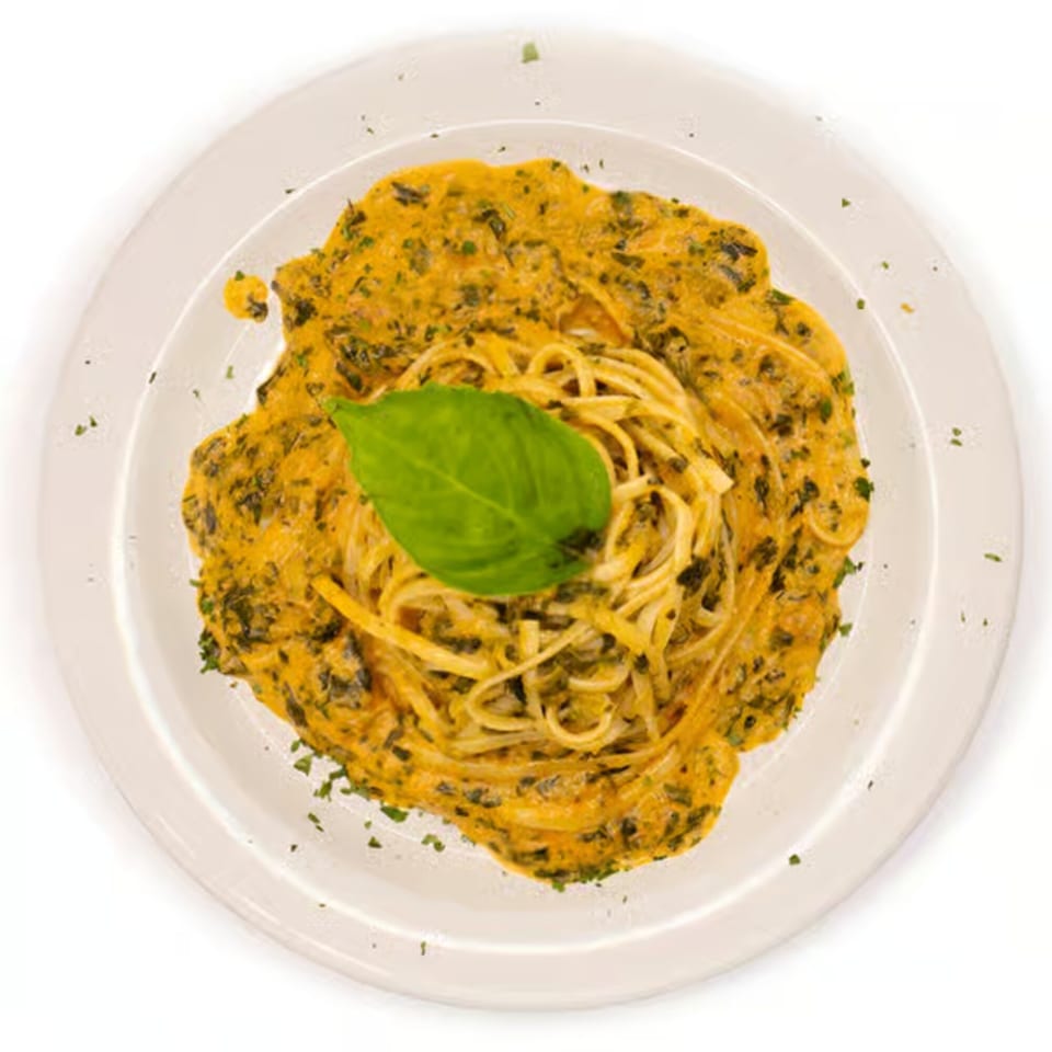 Linguine pasta with a creamy orange sauce and green herbs, garnished with a fresh basil leaf.